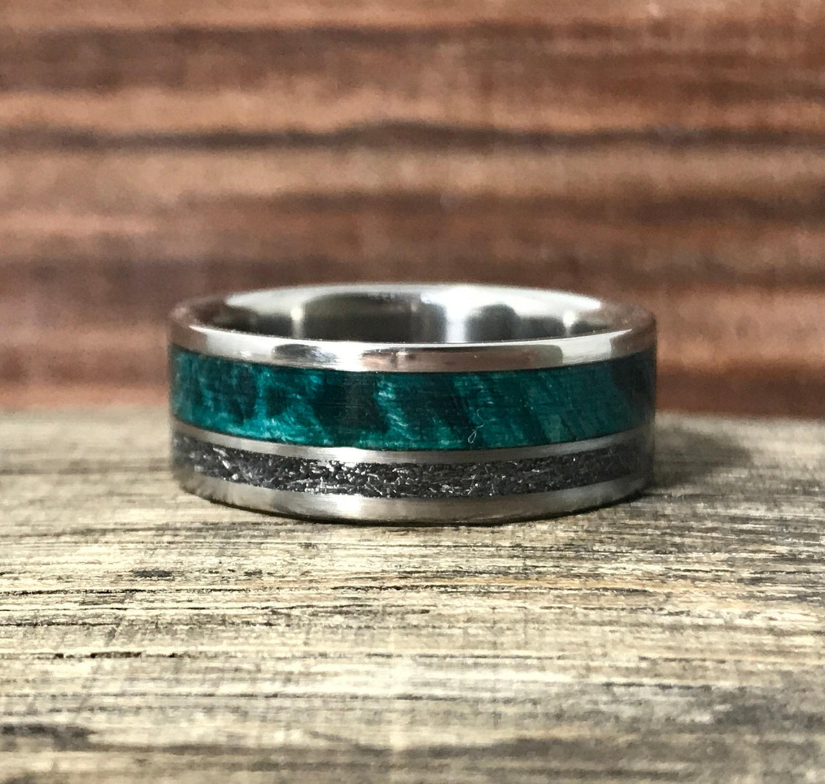 The ring rests flat on a wooden surface, showing its full band composed of a bright green wood inlay and a textured metallic band.