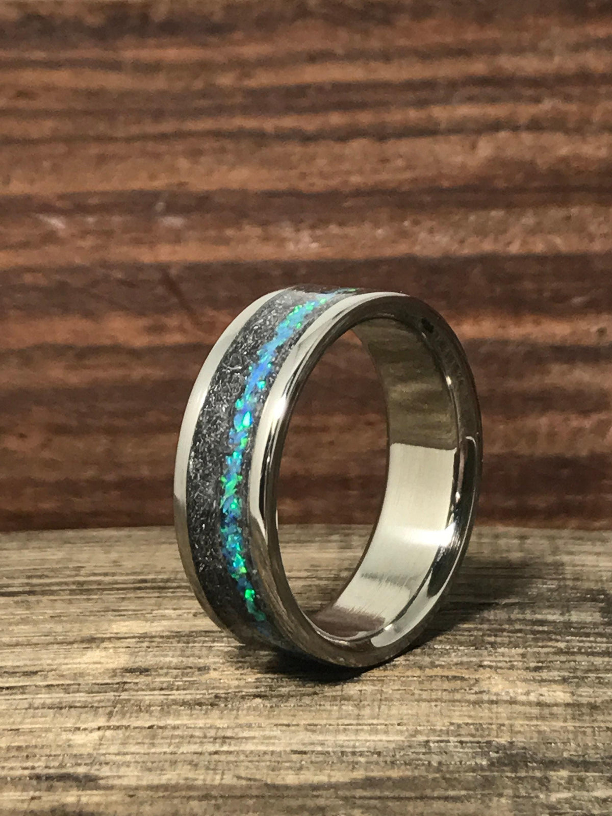 A close-up shot of the ring standing on a wooden surface, showing the contrast between the shiny metal edges and dark inlay.