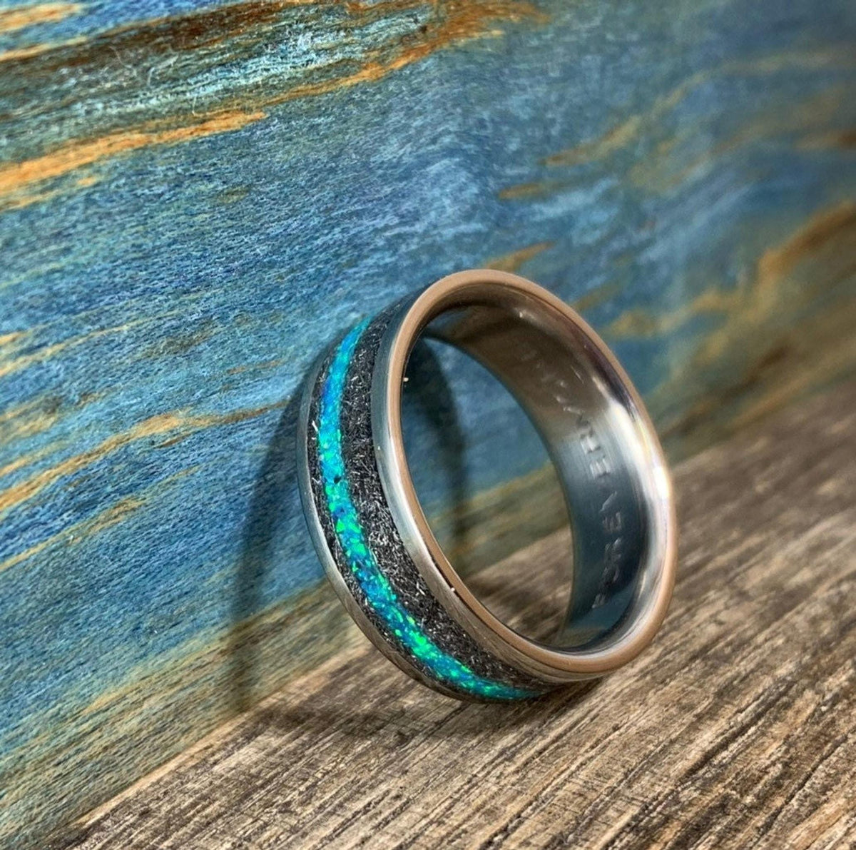 The ring is angled against a rustic blue wood surface, highlighting the shimmering blue opal and meteorite pattern.