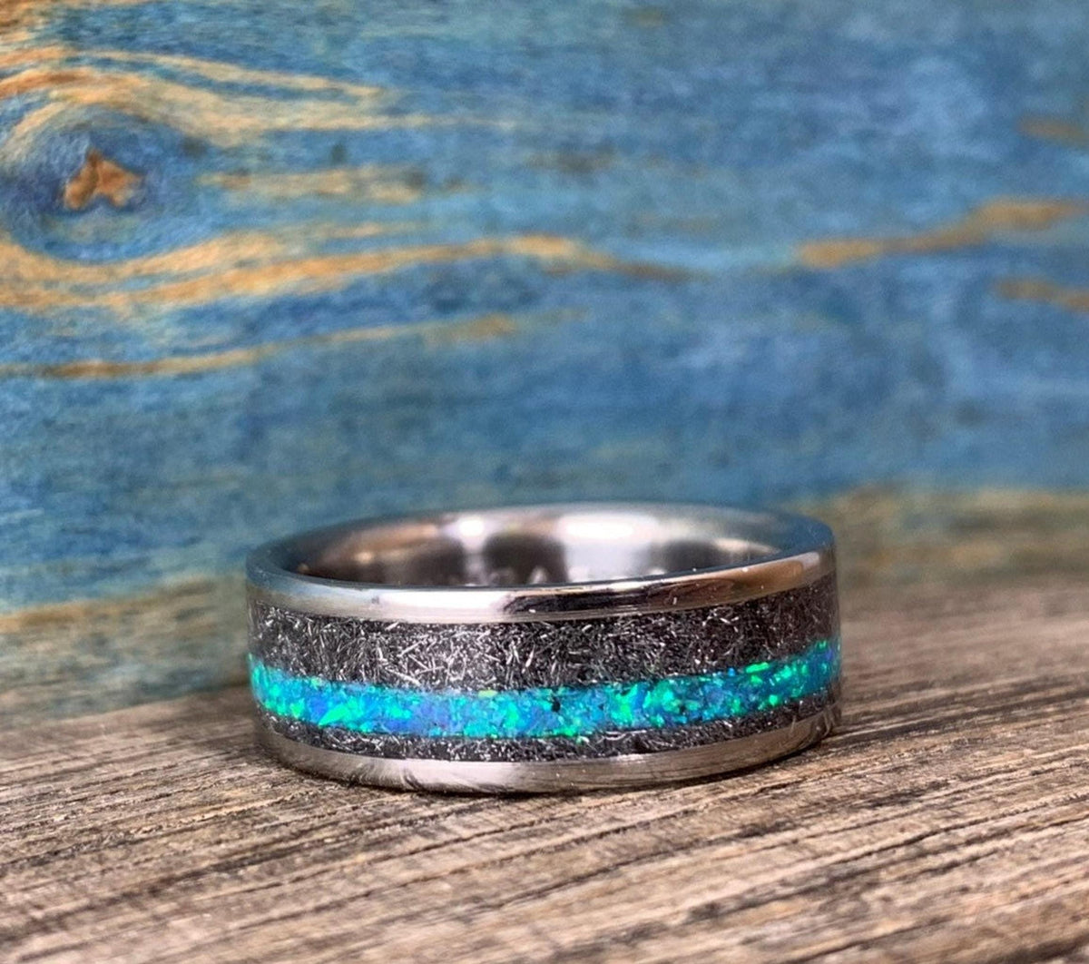 The ring rests horizontally on wood, displaying the continuous band of glowing blue opal fragments and meteorite texture.