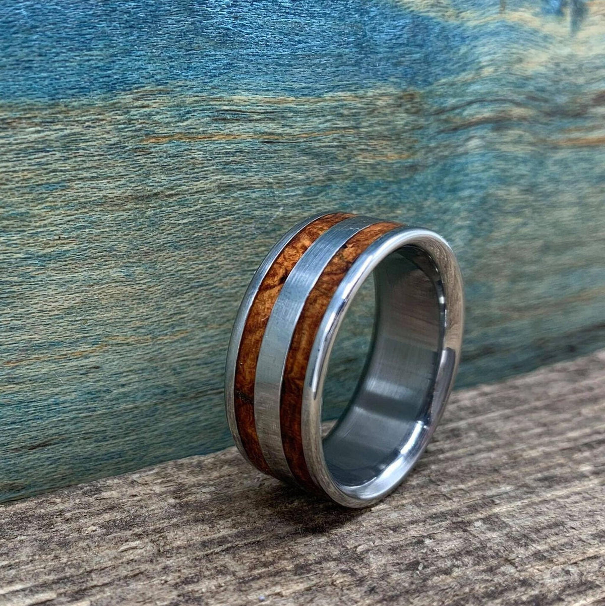 An angled view of the metal and wood inlay ring resting on a weathered wooden surface.