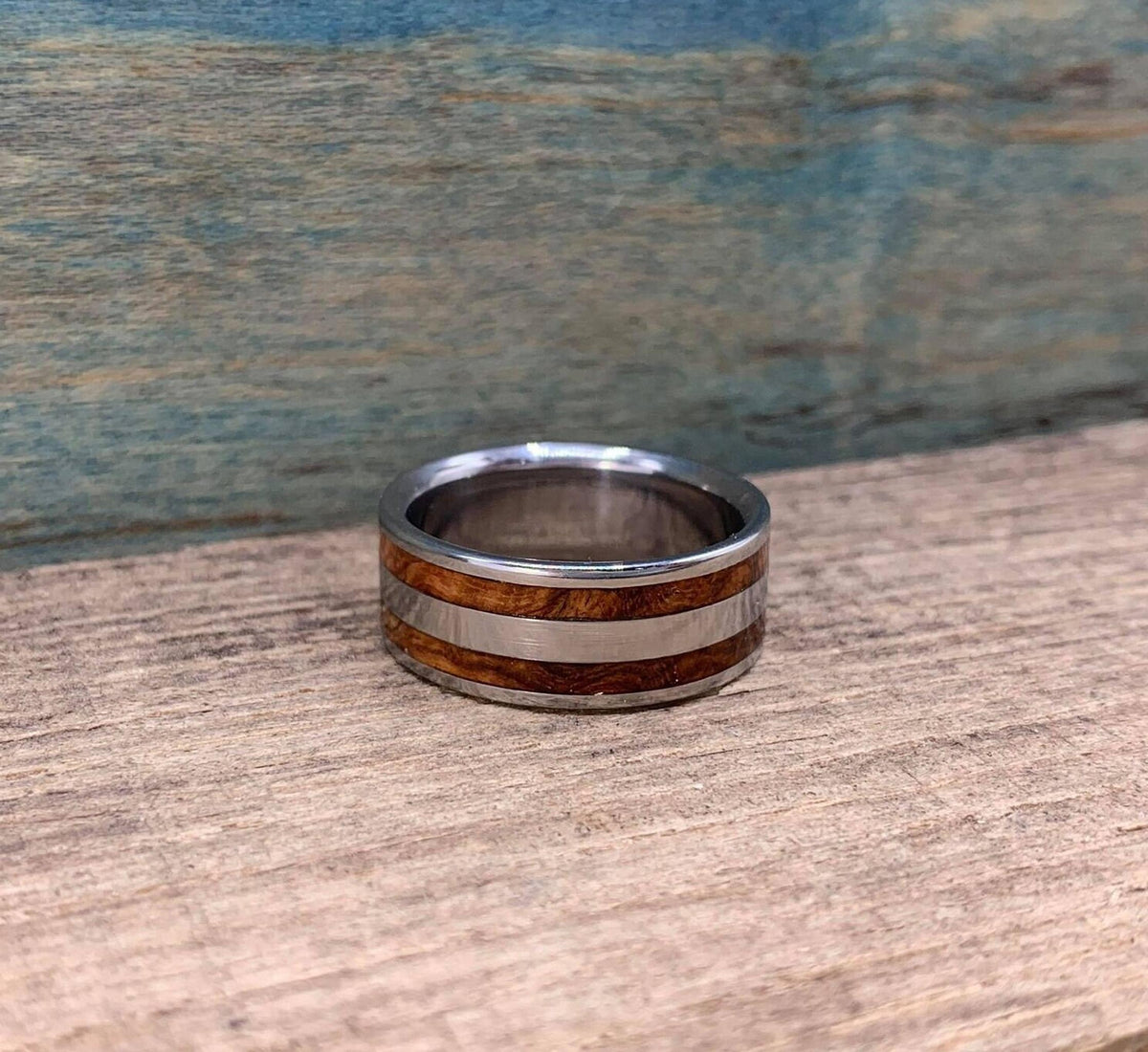 The ring lying flat on the wooden surface, showing its interior and alternating metal and wood bands.