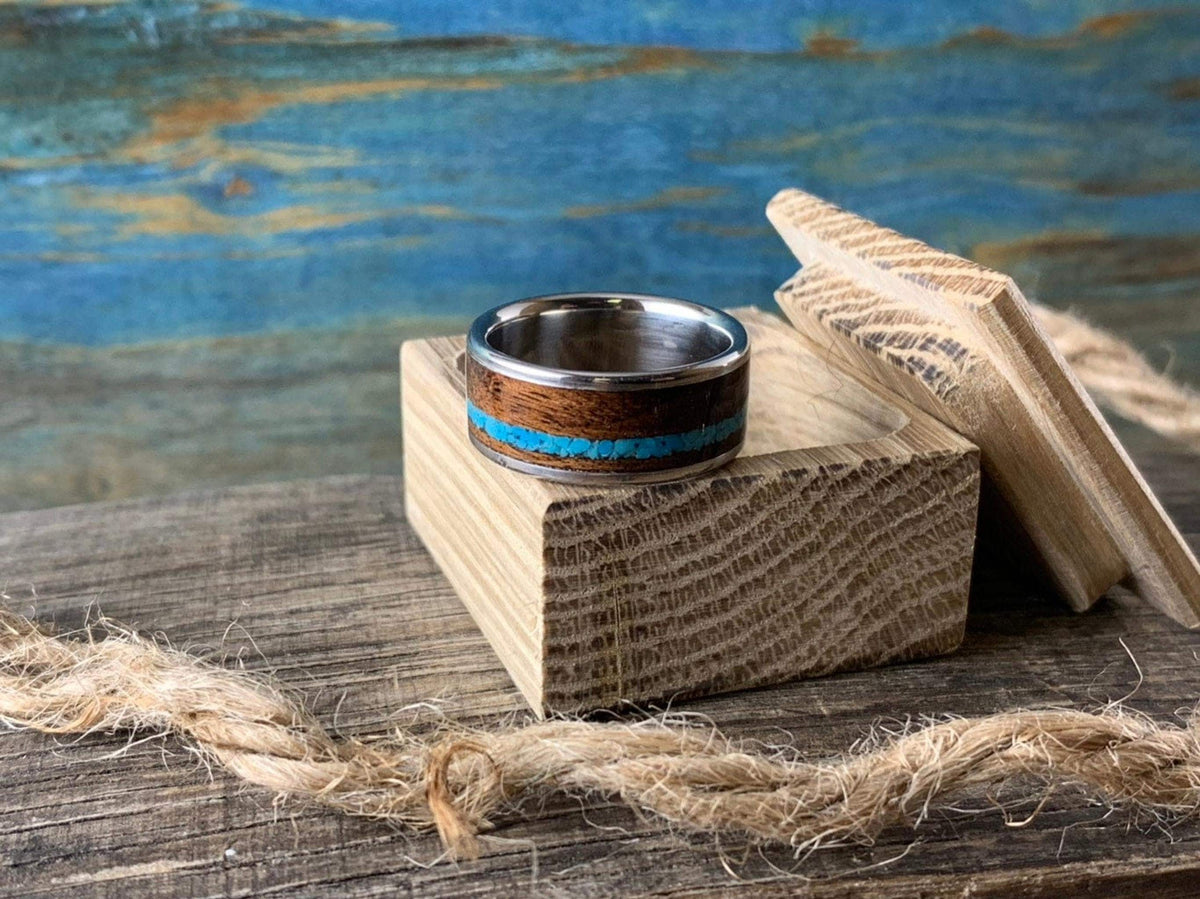 The ring rests next to an open wooden box on a rustic wooden board with twine.