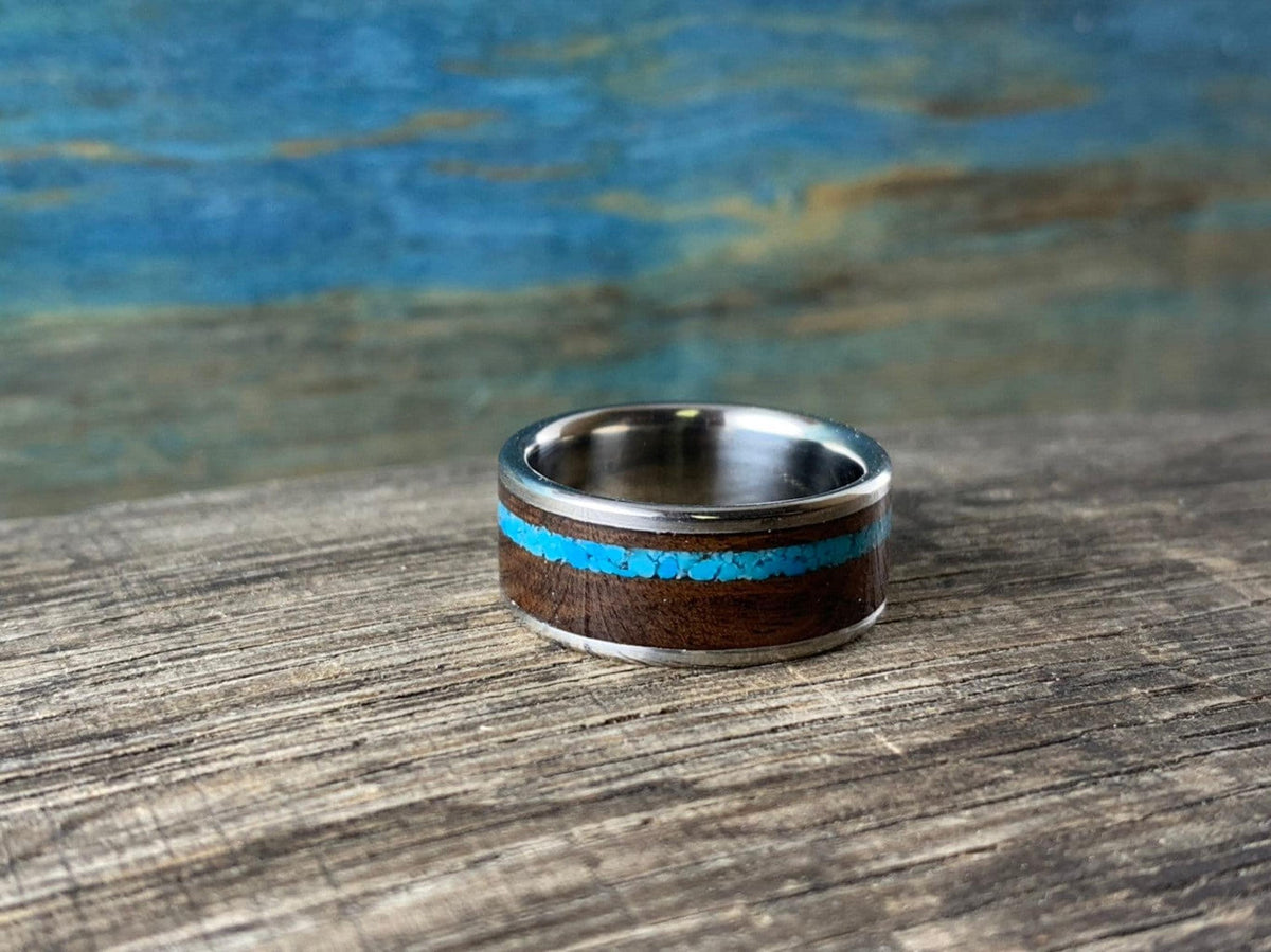The ring rests flat on a rustic wooden surface against a blue-toned textured background.