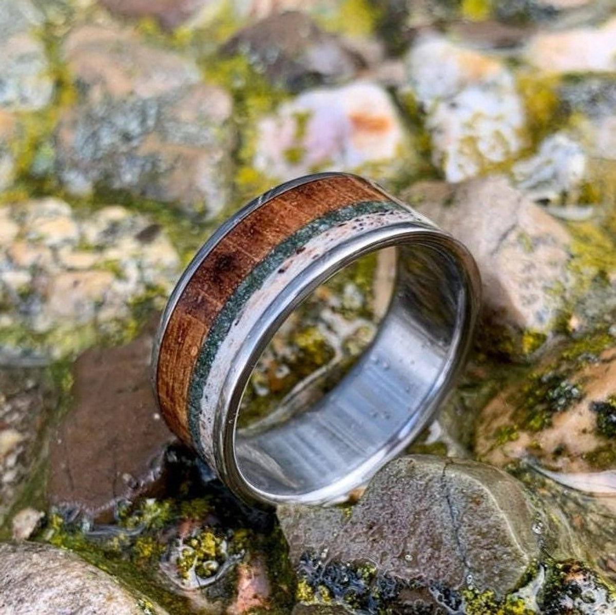 A detailed shot of the ring angled on a rocky background with visible inlays of wood, green stone, and bone.
