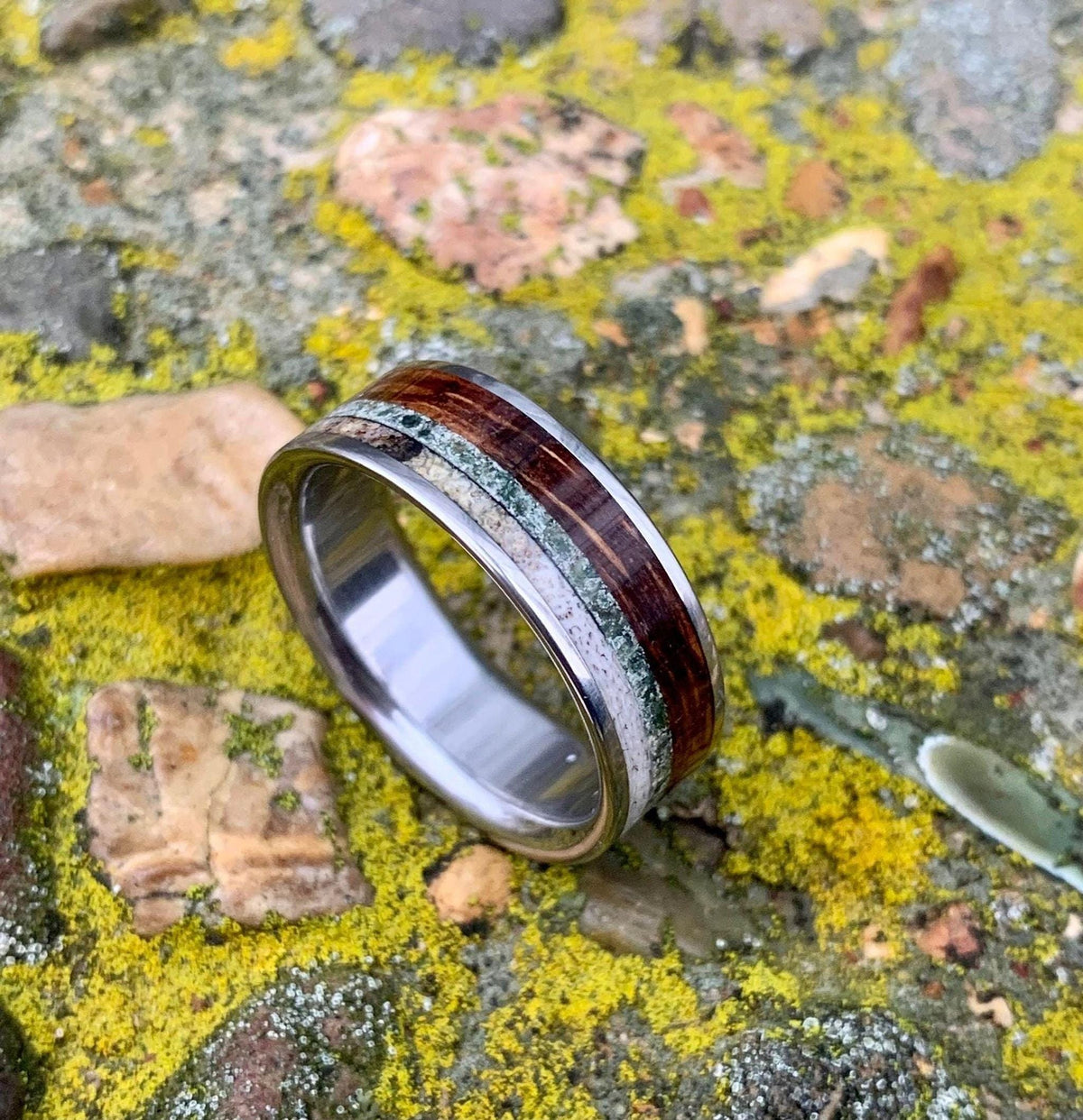 The ring displayed on a textured, moss-covered ground with natural lighting.