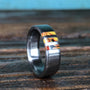 A metal ring with a colorful inlaid segment stands upright on a dark wooden surface.