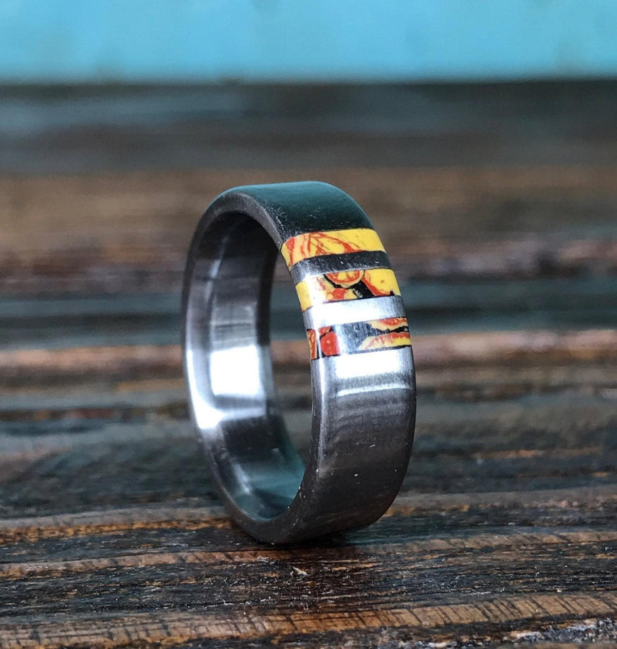 A metal ring with a colorful inlaid segment stands upright on a dark wooden surface.