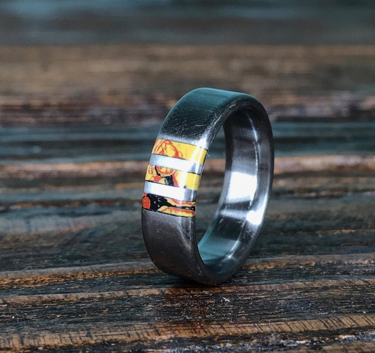 A close-up view of the metal ring standing on a dark wooden surface, focusing on the yellow and red inlay sections.
