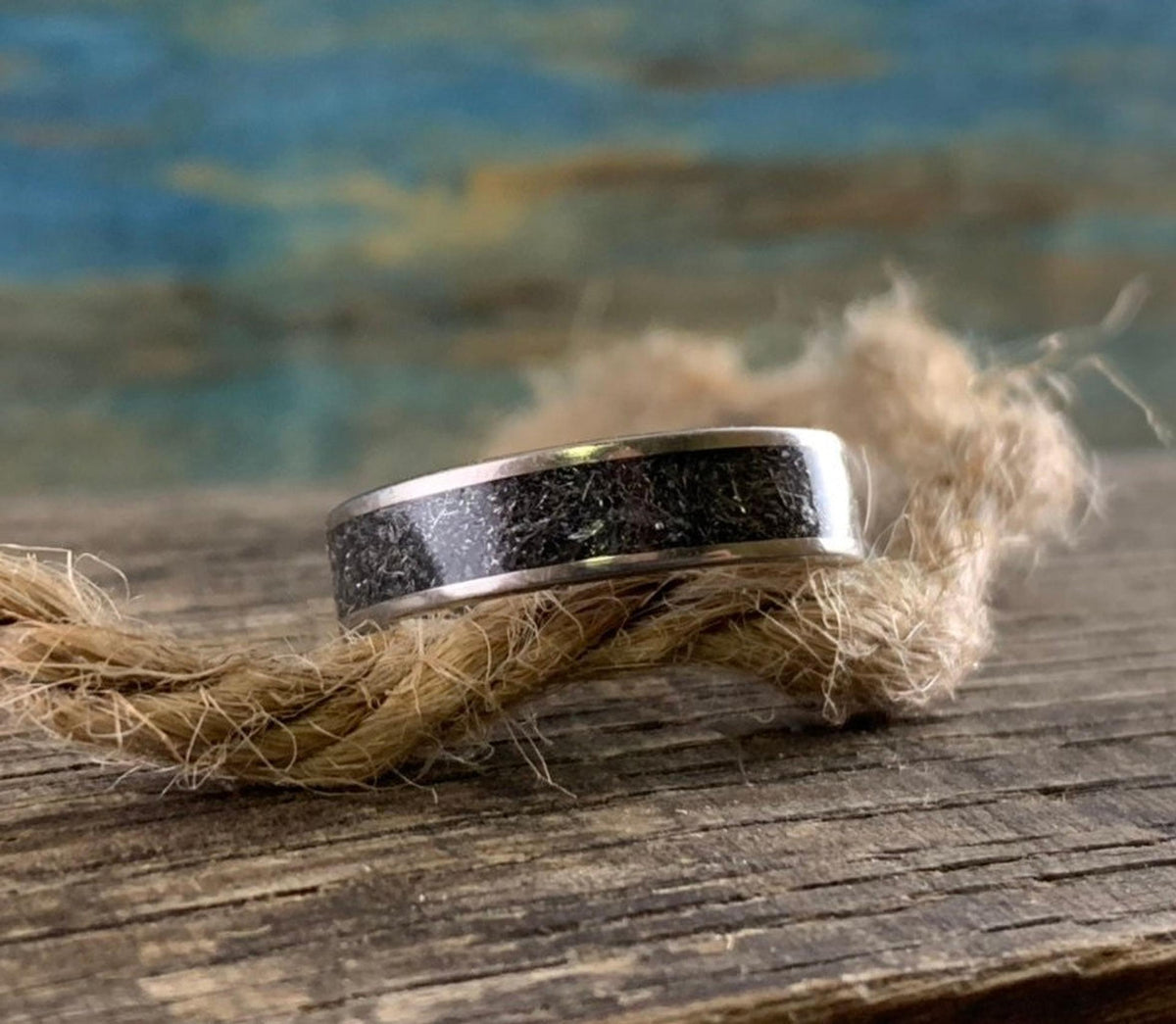 The ring rests horizontally atop a piece of rough jute twine laid across the rustic wood surface.