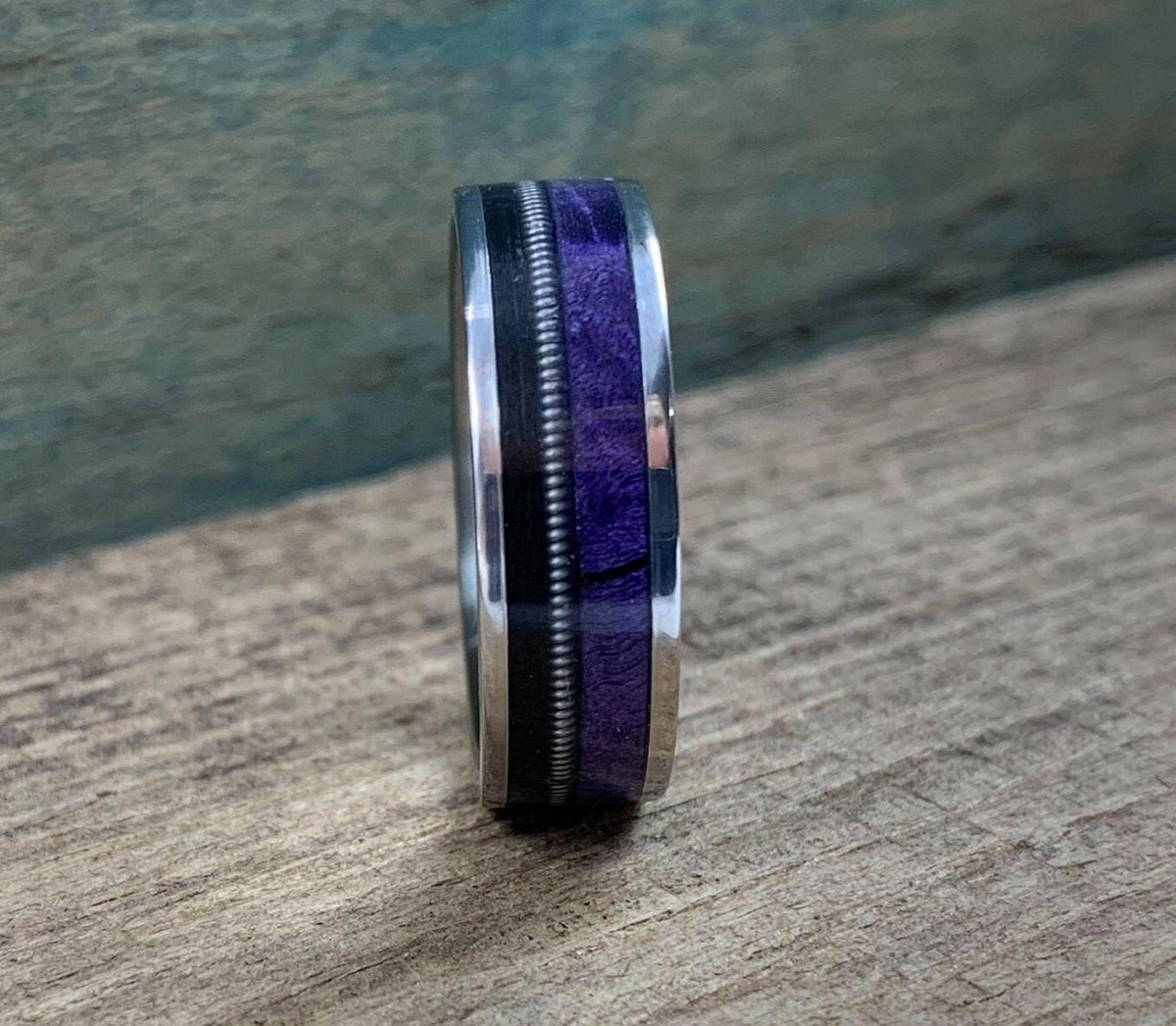 A side profile view of the ring standing upright on a wooden board, highlighting its slim band and inlay details.