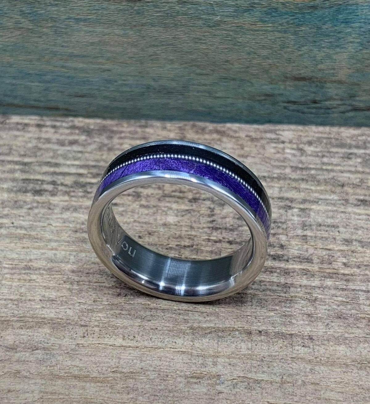 The ring laying flat on a wooden surface, showing the metallic sheen of the guitar string flanked by black and purple inlays.