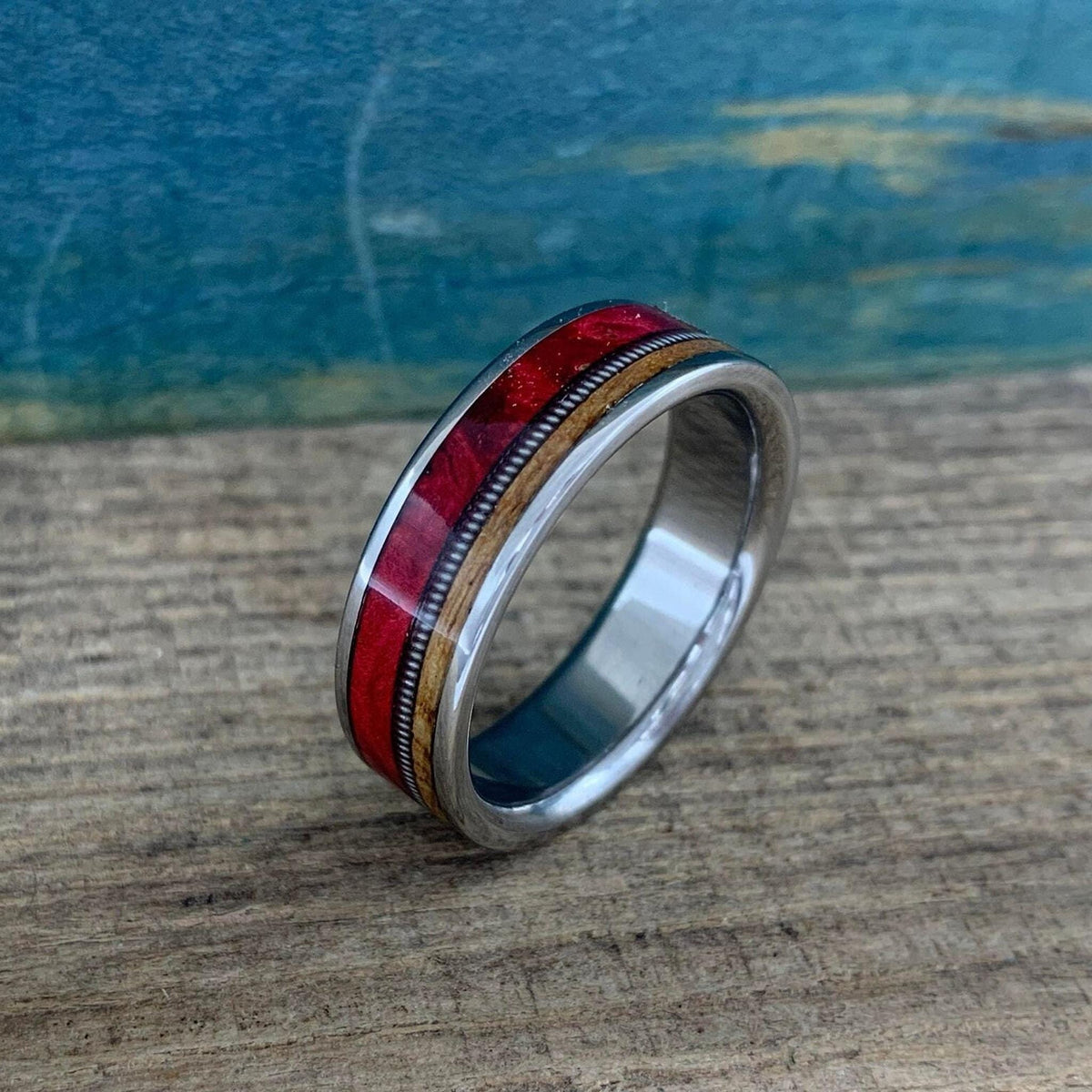 The ring is positioned at a three-quarter angle on a wooden board, highlighting the polished silver interior and the multi-material band details.