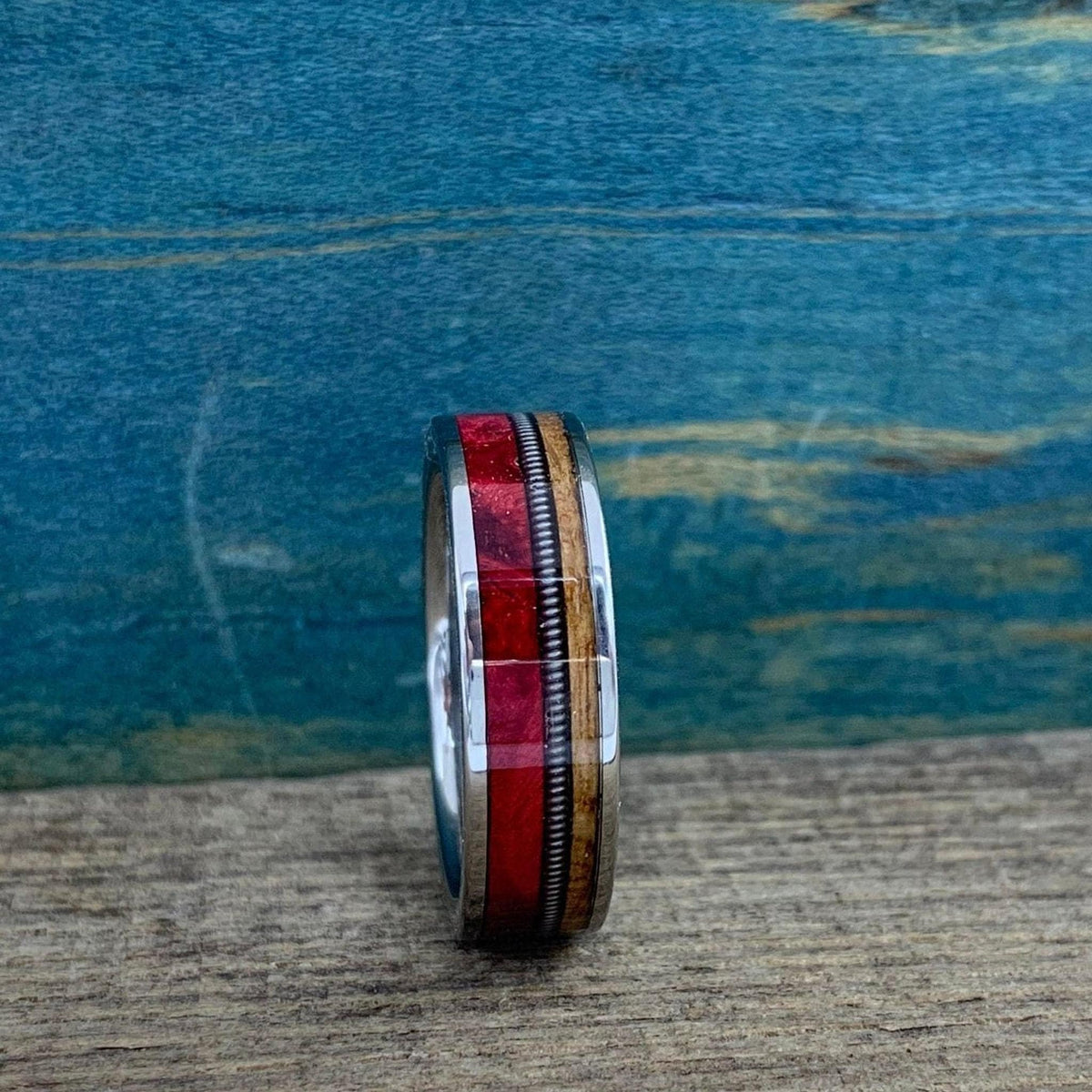 The ring stands vertically, viewed straight-on to showcase the alignment of the vibrant red inlay, metal wire accent, and lighter wooden border.