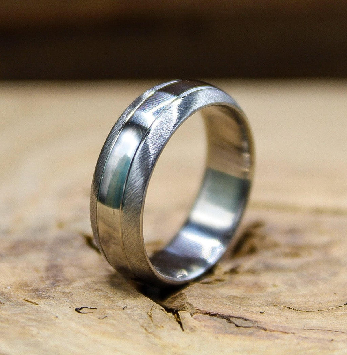 A brushed silver metal band with a shiny central groove shown at an angle on a wooden surface.