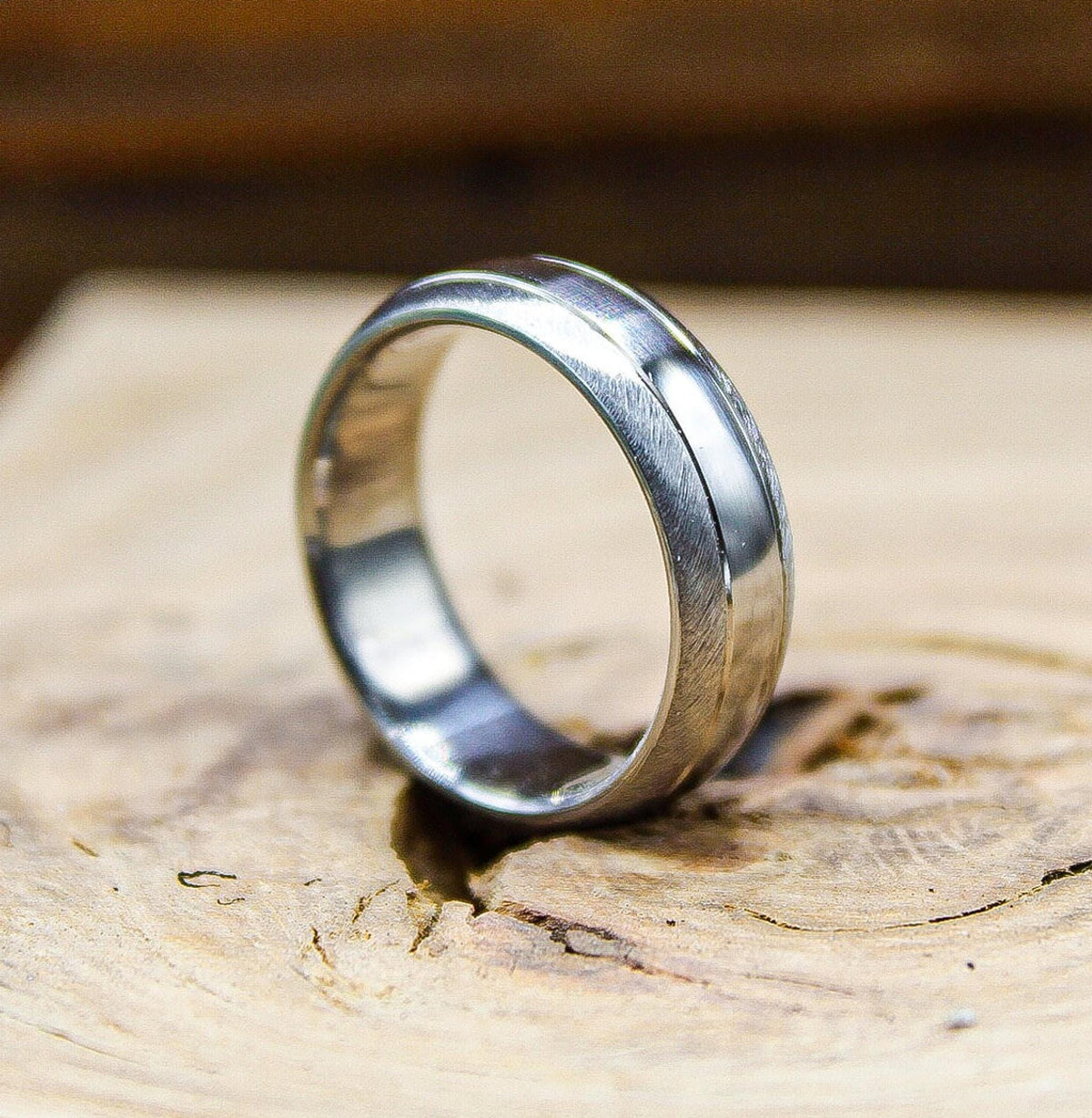 A silver ring with a textured matte exterior and a glossy center stripe angled on a rustic wooden block.