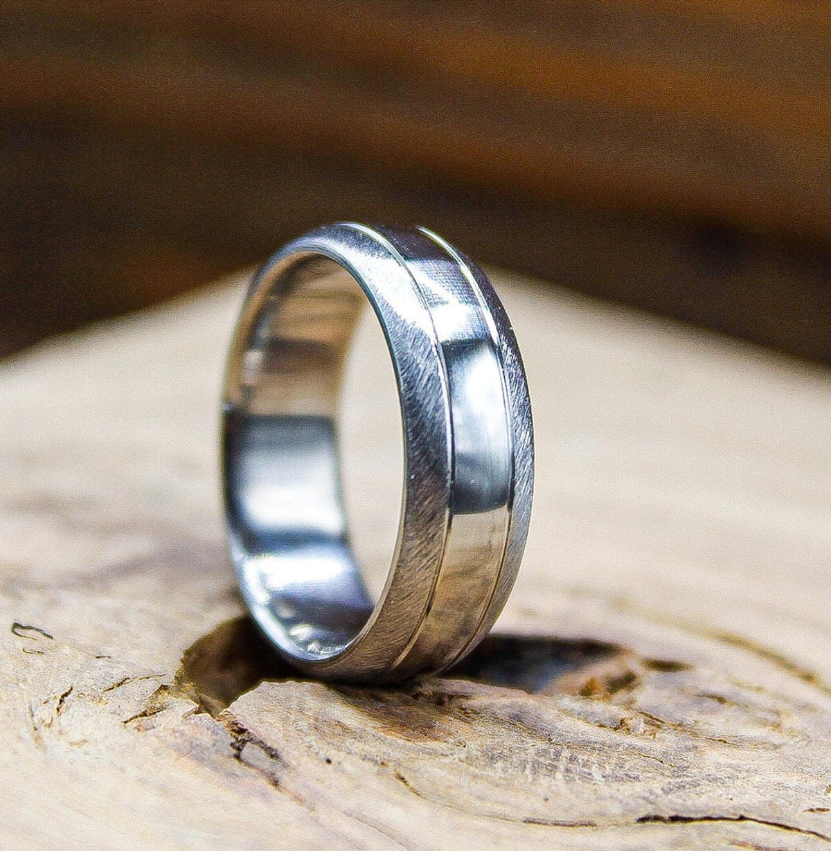 A silver-colored ring displaying a brushed texture alongside a shiny center band standing on a wooden surface.