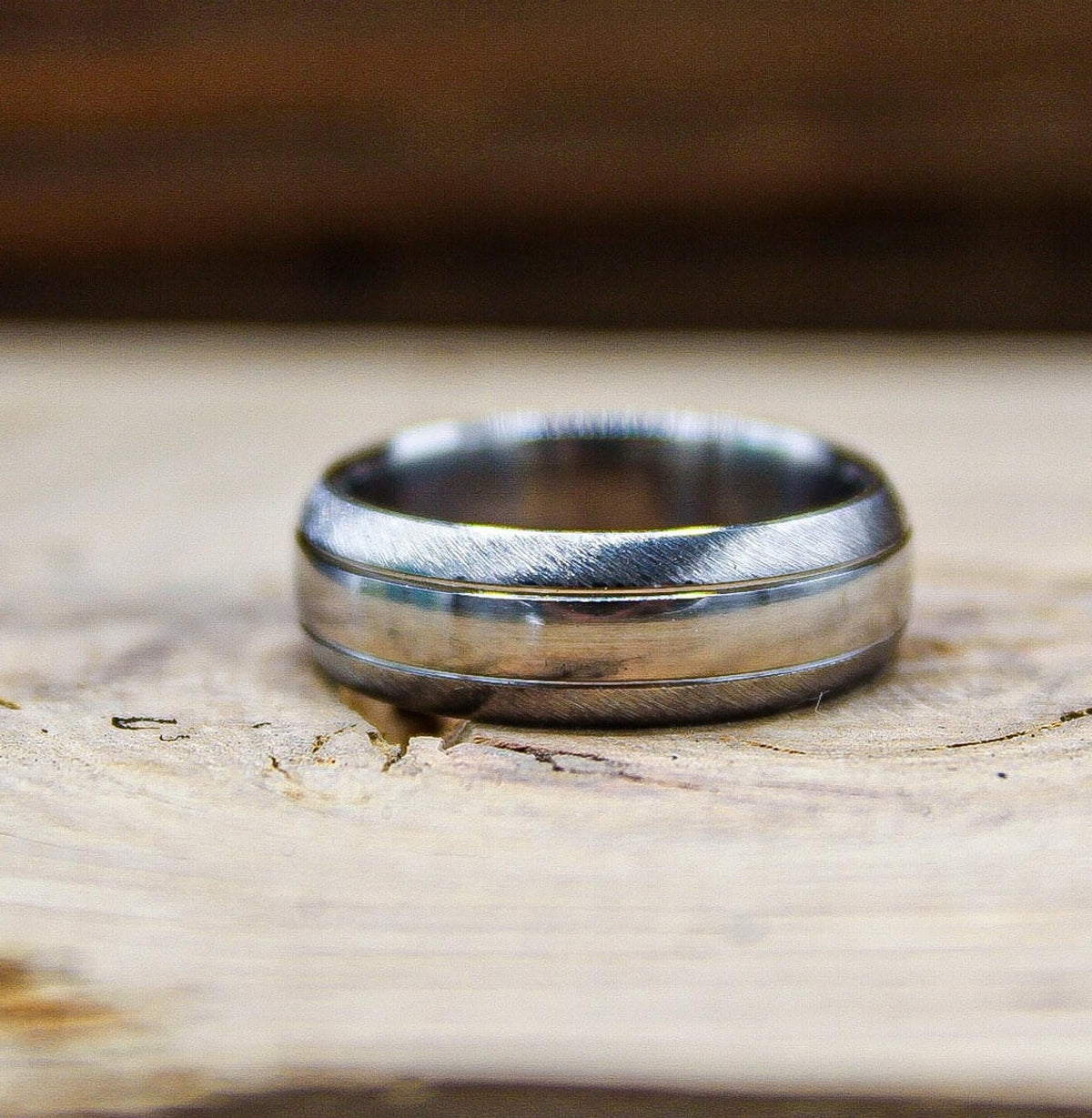 A silver ring with a brushed texture and polished central stripe resting flat on a wooden surface.
