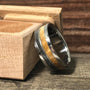 A band ring with metal, wood, and meteorite inlays leaning against an open wooden box on a rustic wood surface.