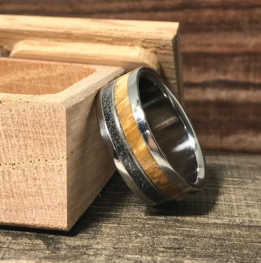 A band ring with metal, wood, and meteorite inlays leaning against an open wooden box on a rustic wood surface.