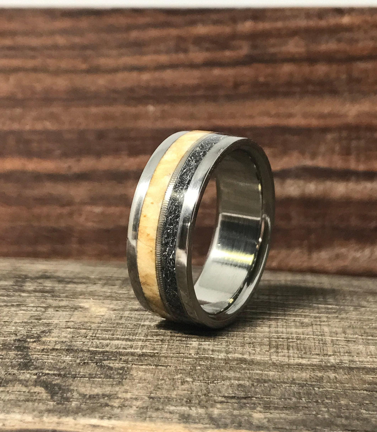A multi-material wedding band standing on a rustic wooden table with a dark grain backdrop.