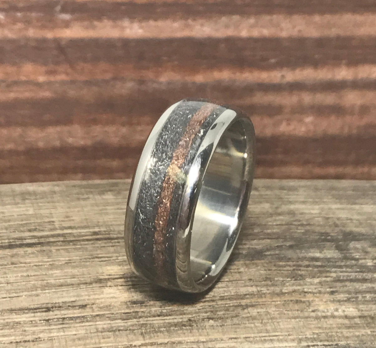 A close-up profile of the titanium, meteorite, and rose gold ring angled on a weathered wooden plank.