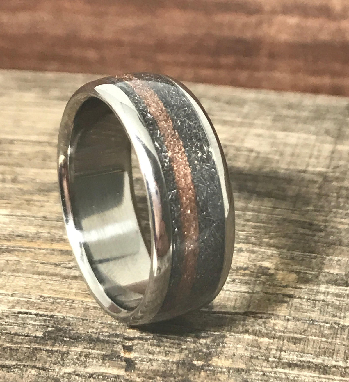 The titanium ring standing upright at a slight angle on a textured wooden board.