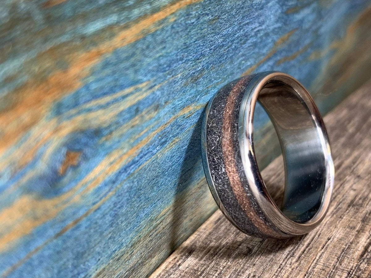 The titanium ring with meteorite and rose gold inlay leaning slightly against a blue and brown textured wooden backdrop.