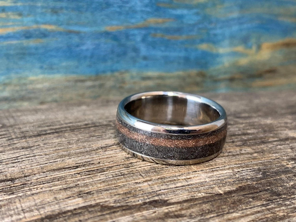 The titanium ring lying flat on its side on a wooden surface, showing its interior finish and the outer rose gold and meteorite inlays.