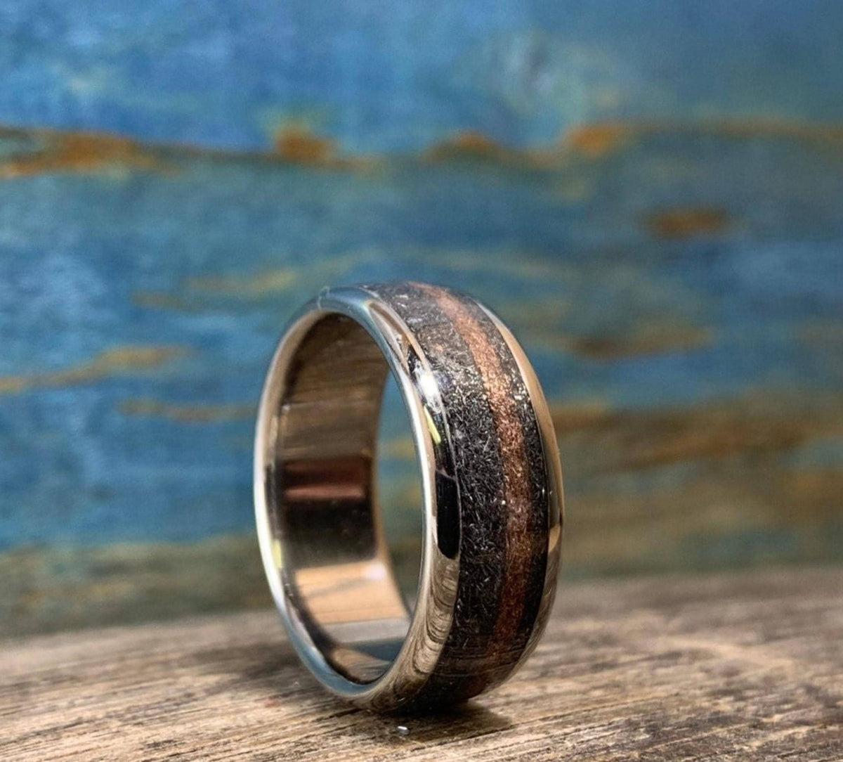 An angled view of the titanium ring showing the polished metal edges, meteorite inlay, and central rose gold stripe.