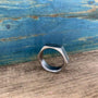 A hexagonal metal ring rests on a wooden surface against a blue textured backdrop.