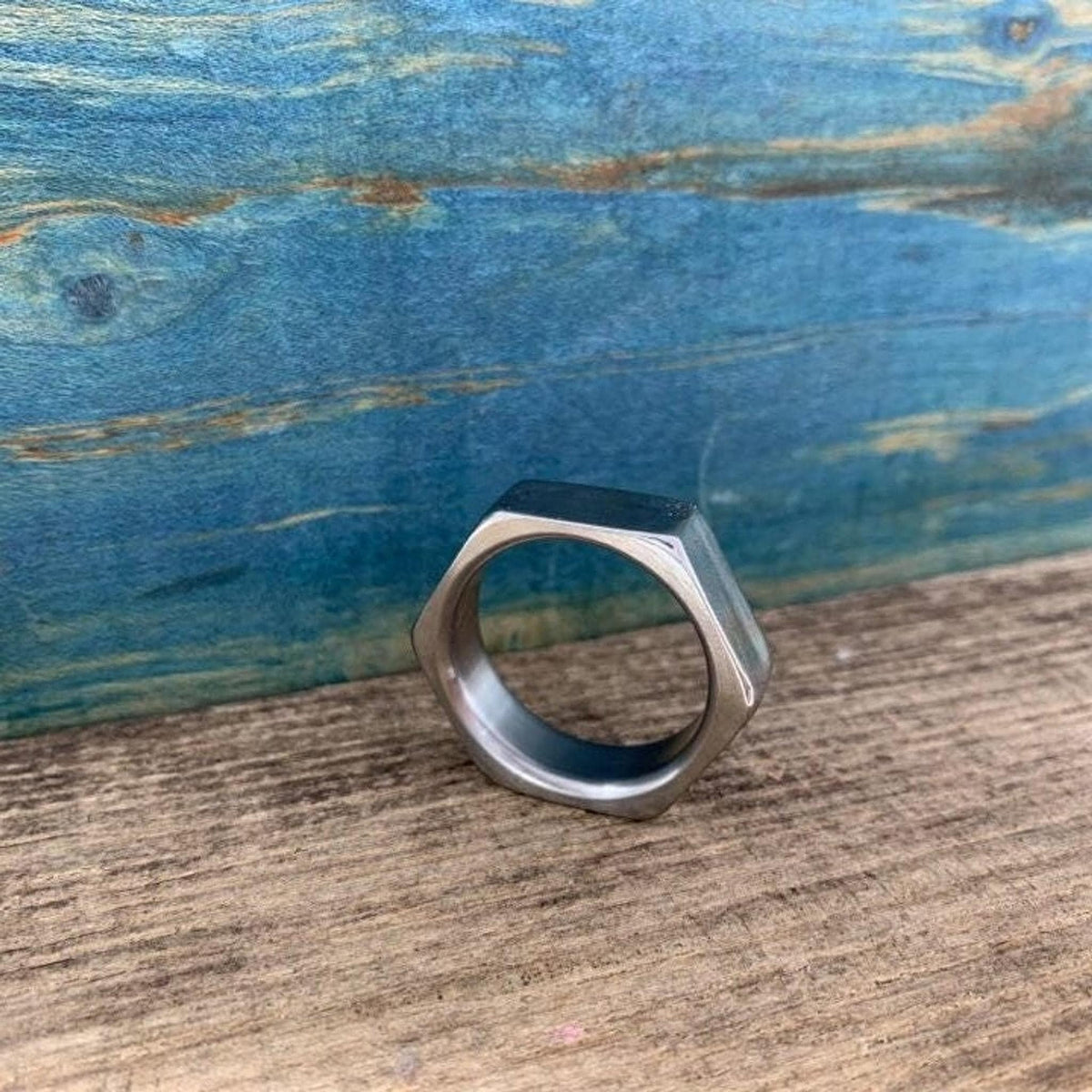 A hexagonal metal ring rests on a wooden surface against a blue textured backdrop.
