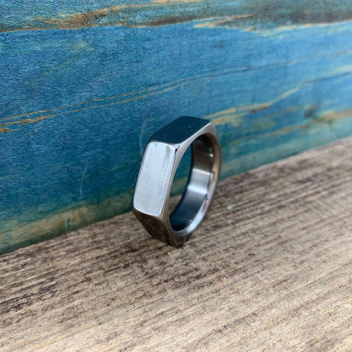 A silver-colored hexagonal band angled on wood with a blue background.