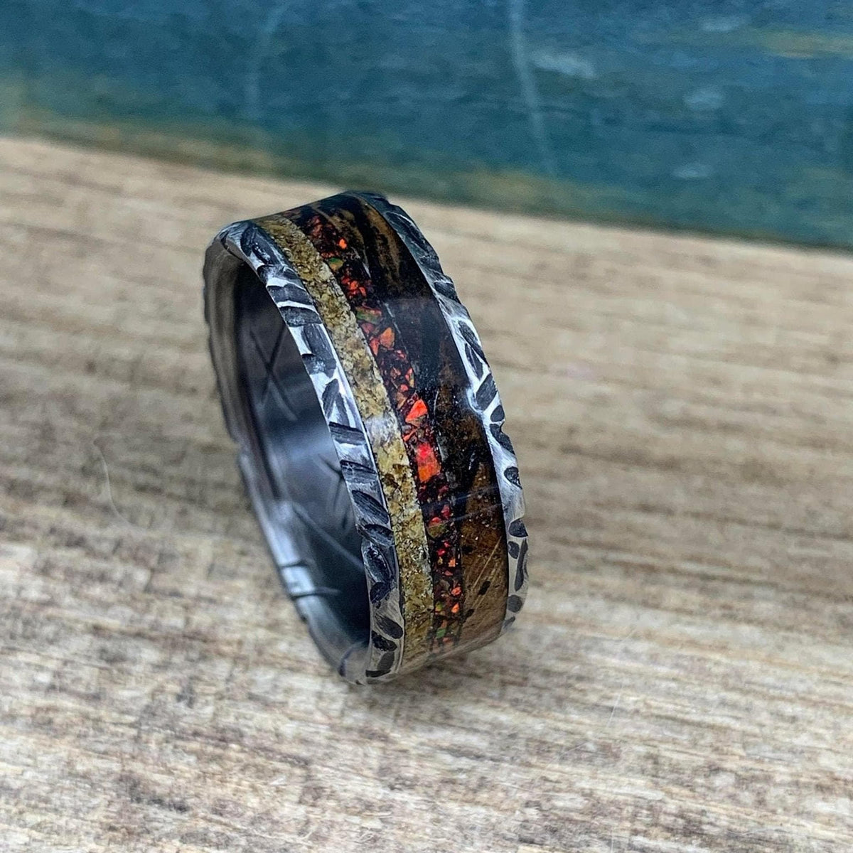 A close-up of the textured ring turned slightly to display the red and gold inlay details.