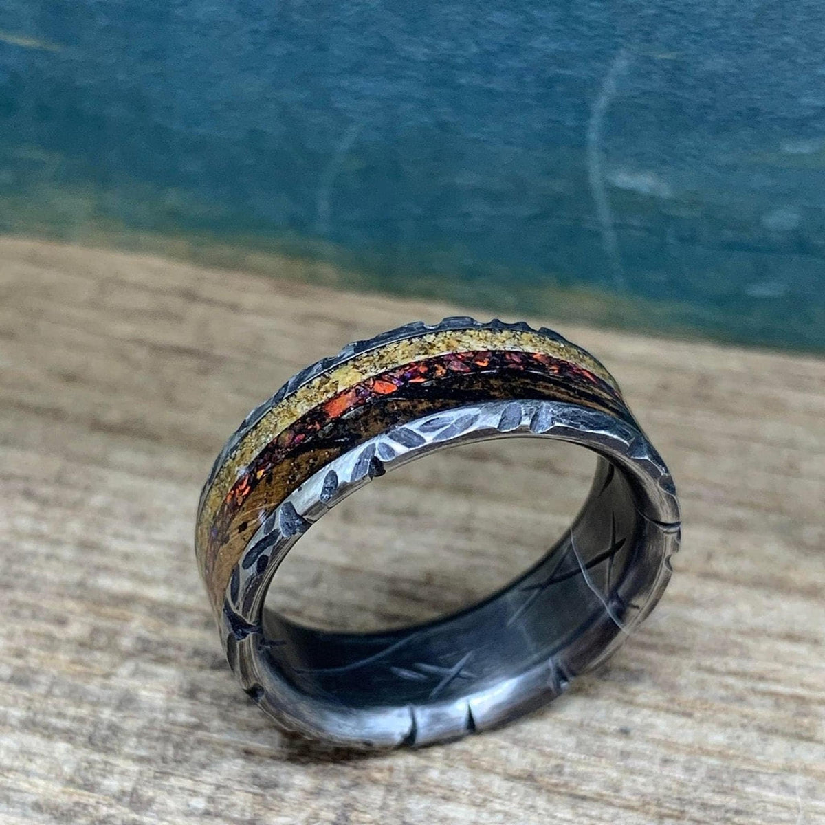A slightly closer perspective of the textured wedding band resting on wood against a mottled blue background.