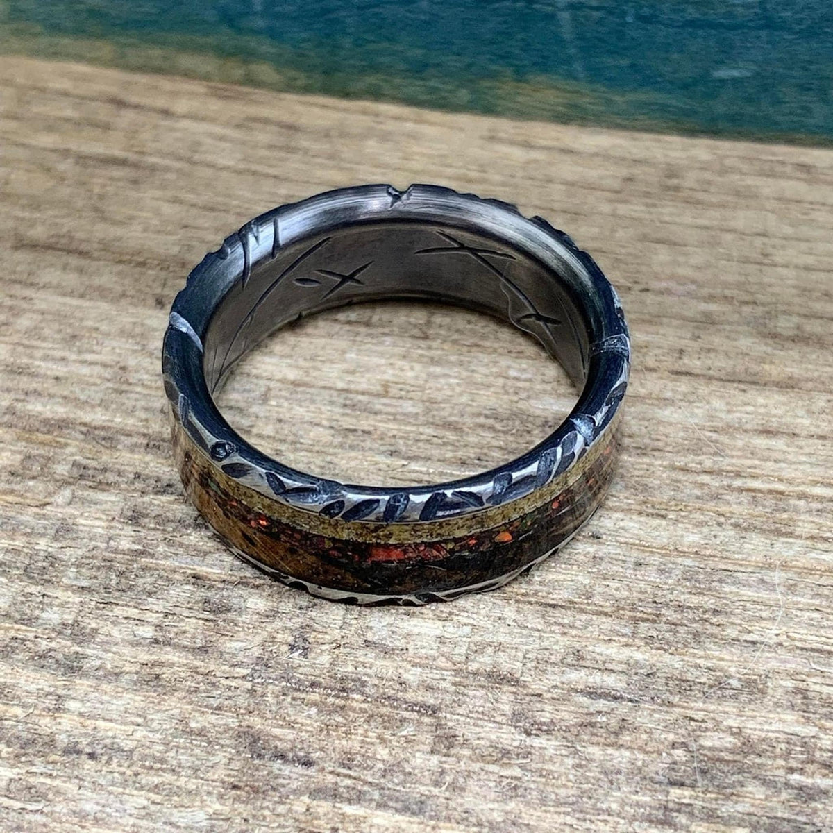 The wedding band laying flat with the inlay facing downward, revealing carved runes inside the dark band.