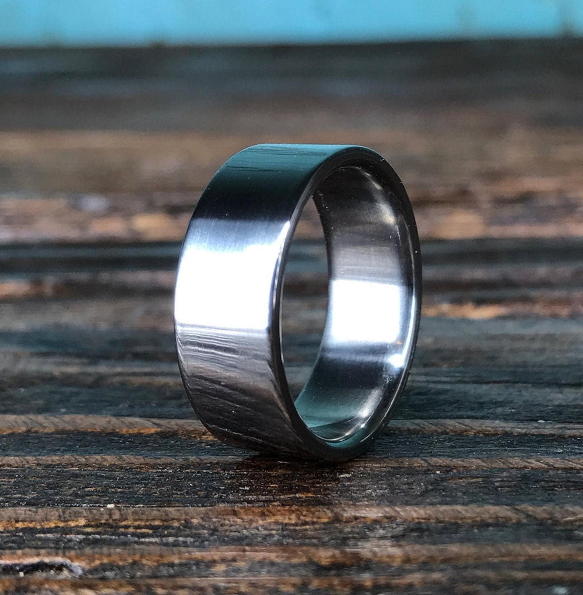 A wide polished metallic band stands upright on a dark wooden surface.