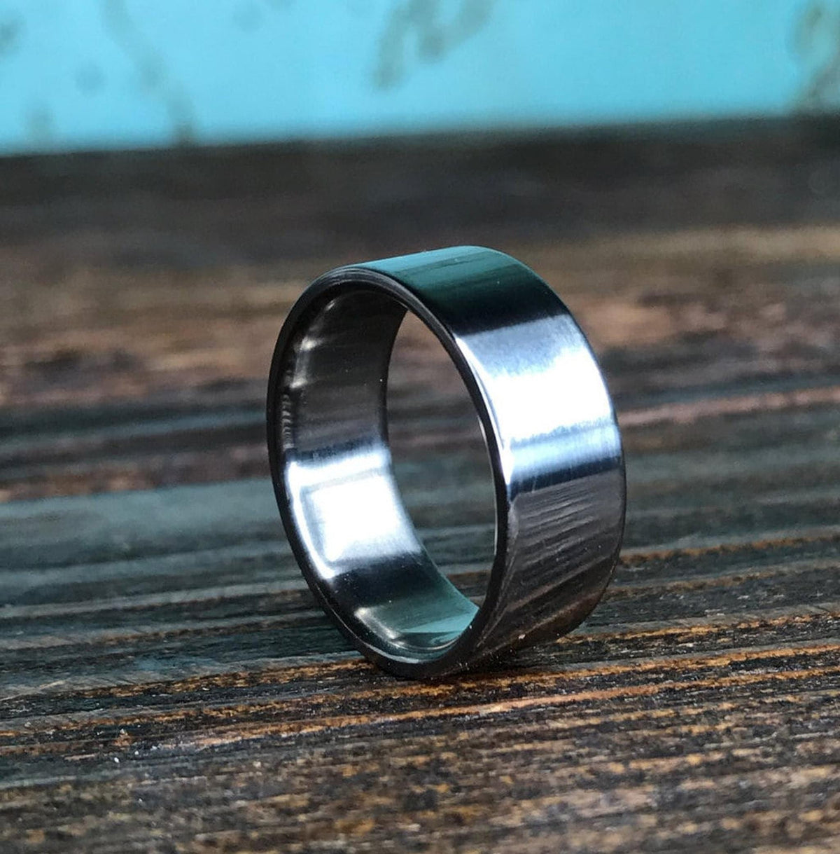 A metallic ring stands on edge showing its polished finish against a dark textured background.