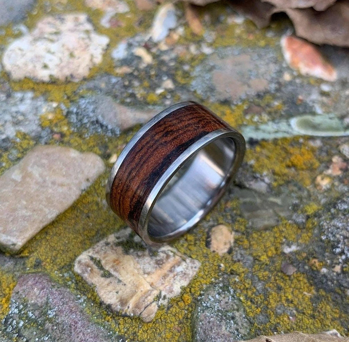 A close-up of a wooden inlay ring on a mossy stone surface.