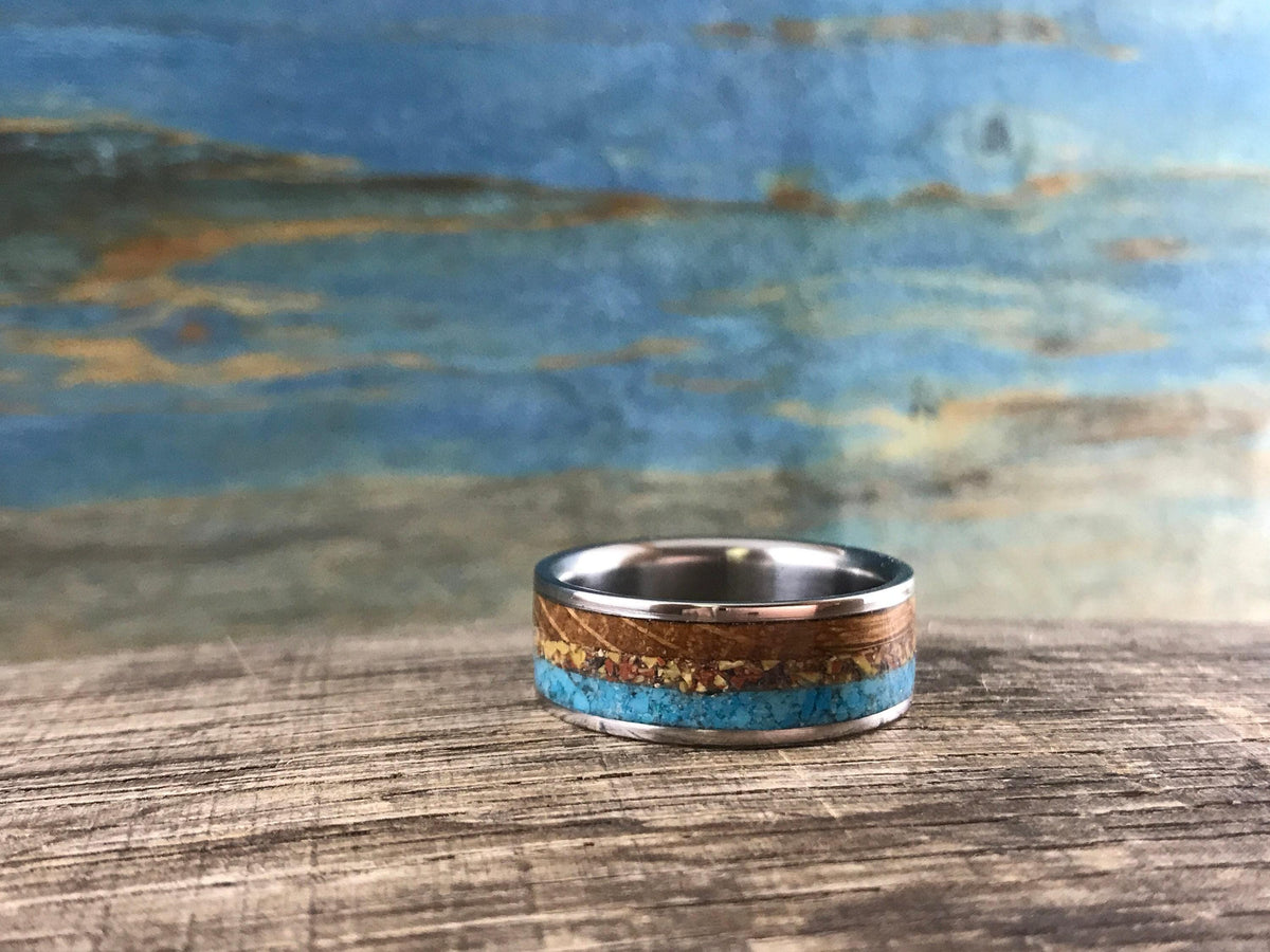 An inlaid ring rests horizontally on a textured wooden surface in front of a blue background.