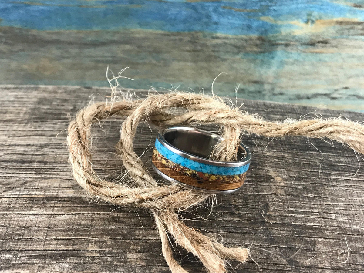 A ring with multi-colored inlay is encircled by a length of rough twine on a weathered wooden plank.