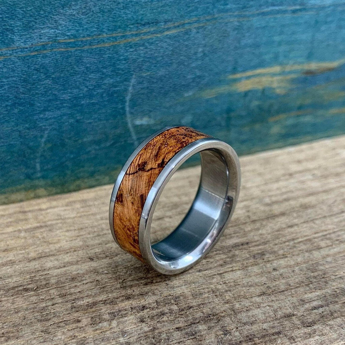 A silver metal ring with a brown wood inlay sitting at an angle on a wooden surface.