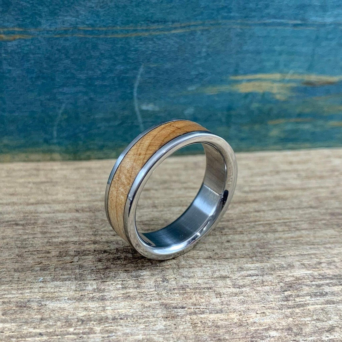 A metallic ring with a wooden accent inlay stands upright on a wooden board.