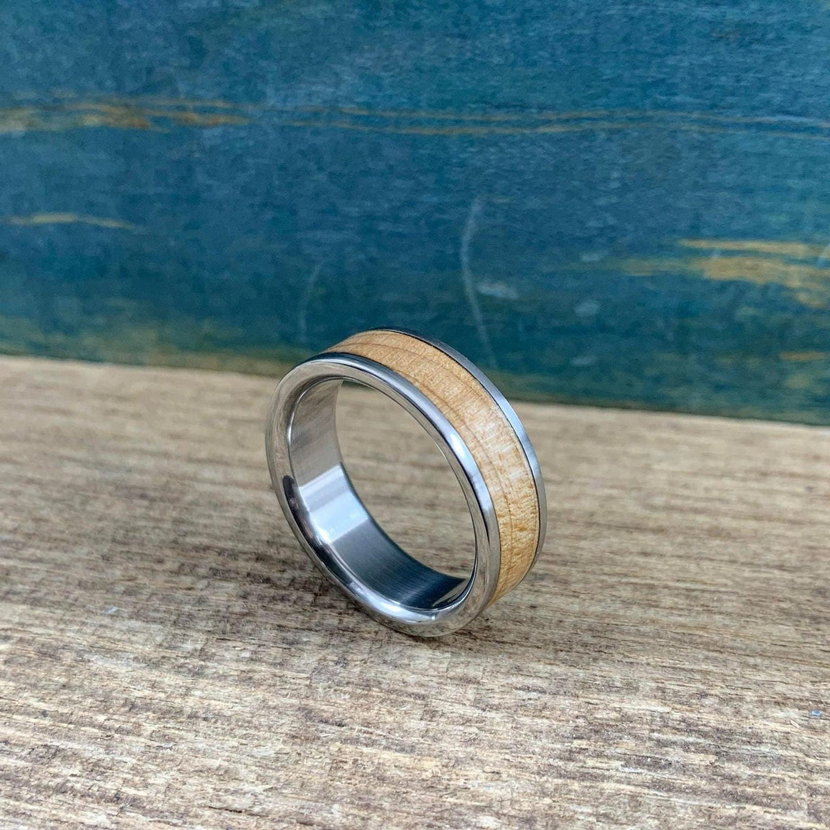 A metallic band with a wood inlay stands upright, angled slightly on a textured wooden surface.