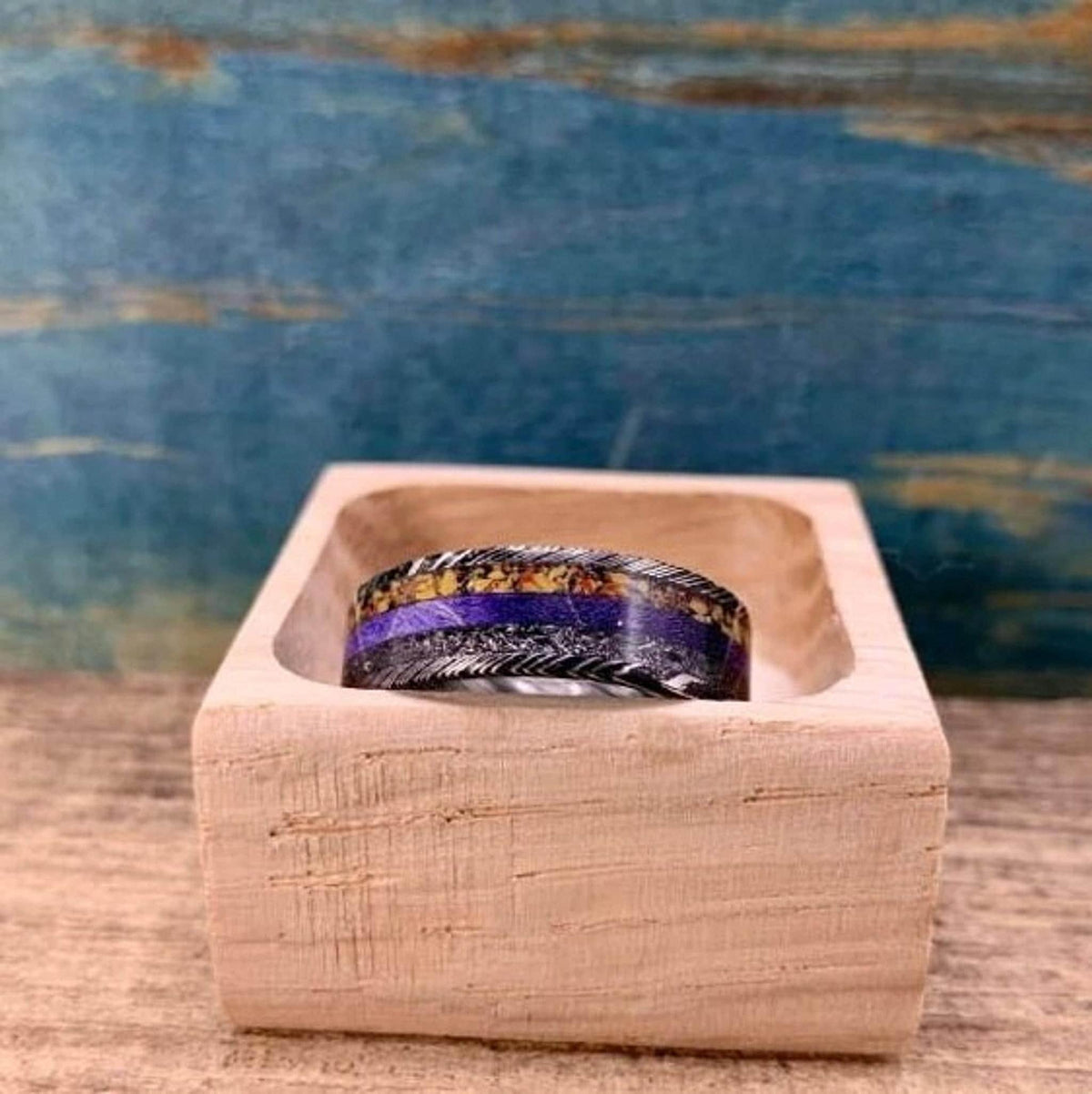 The ring displayed upright inside a small open wooden box on a wooden surface.