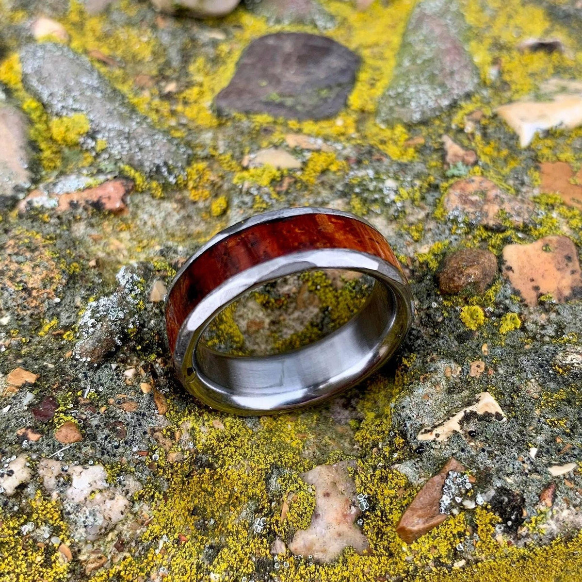 The titanium ring resting on its side on a weathered, mossy stone background.