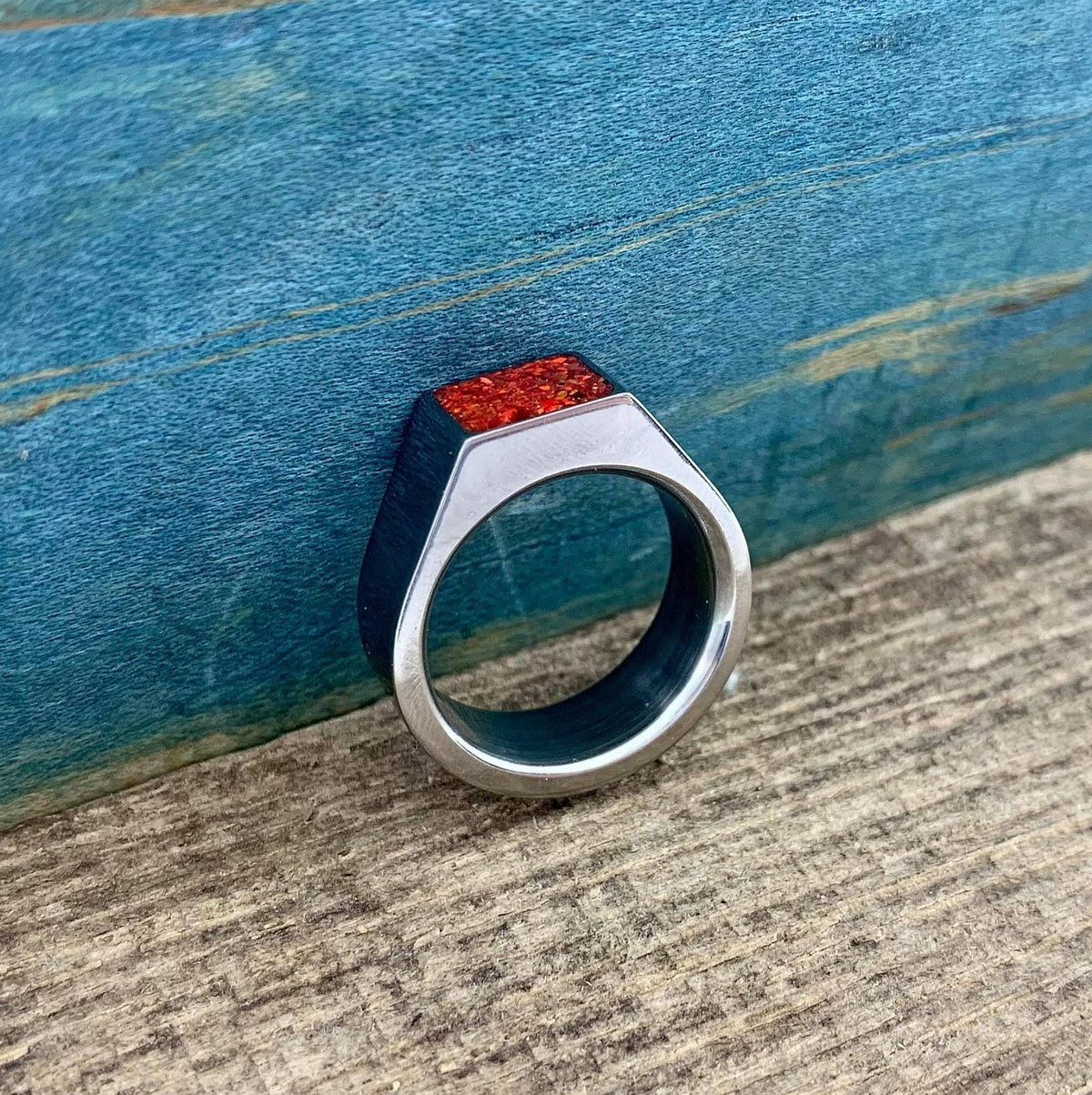 A silver ring with an orange opal face is positioned upright against a rustic blue and brown background.