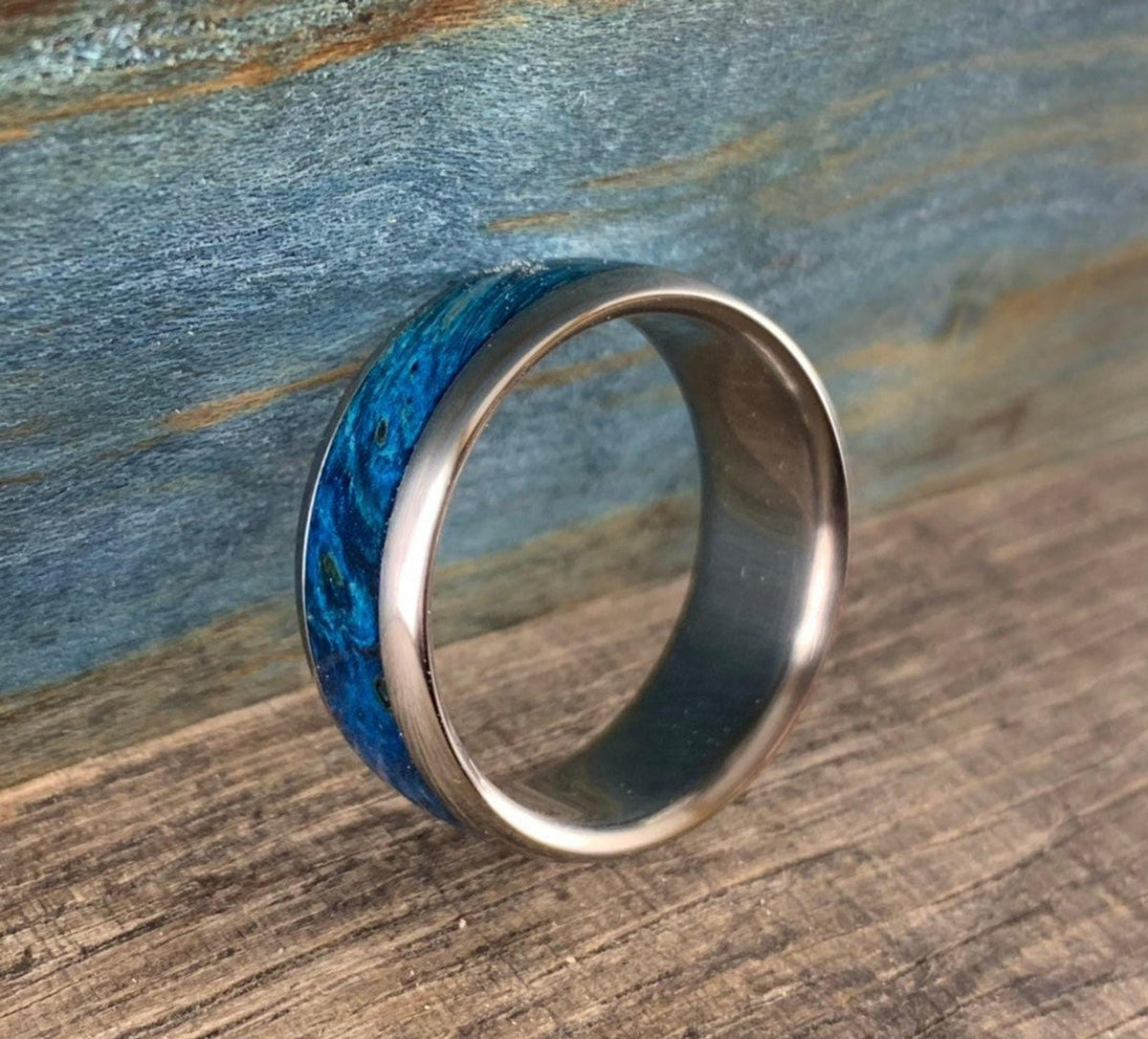 The ring stands on its edge, displaying the rich blue burl wood grain wrapped around the metal band.