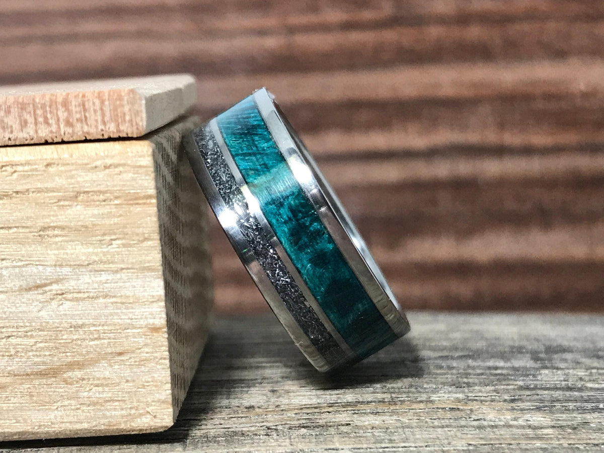 The ring is angled against the side of a small wooden block, highlighting the polished silver edges and colorful inlays.