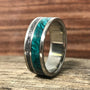 A silver-colored ring standing upright on a wooden surface, featuring a textured metallic inlay beside a vibrant green wood inlay.